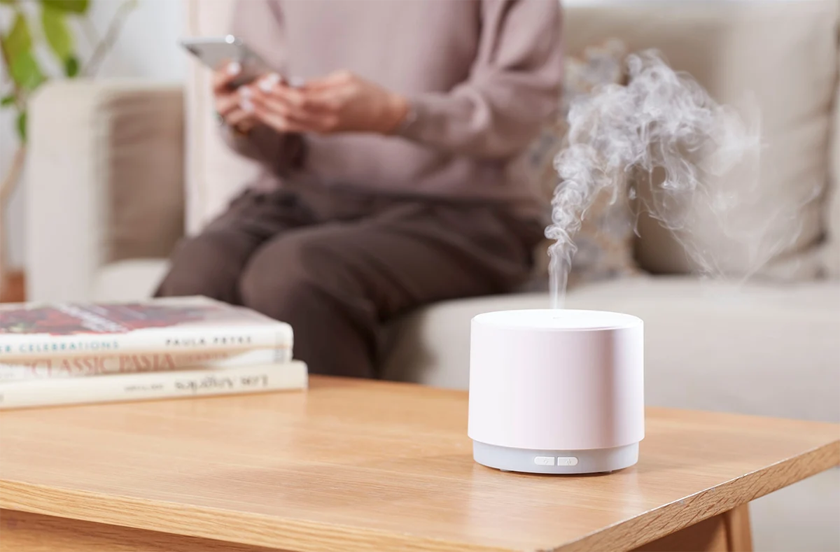 Humidifier releasing mist on a wooden table to help relieve dry winter skin indoors